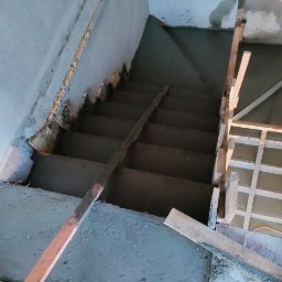 Kompleksowe usługi ogólnobudowlane - Wylewka betonowa na schodach z drewnianym szalunkiem. Widok z góry na betonowe stopnie w trakcie prac wykończeniowych. Szare ściany i fragmenty drewnianych elementów.