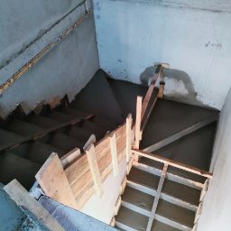 Kompleksowe usługi ogólnobudowlane - Wypełnione betonem schody w surowym stanie, widok z góry. Szalunki z desek. Widoczne niedoskonałości betonu i ślady po szalunkach. Surowe ściany z betonu.