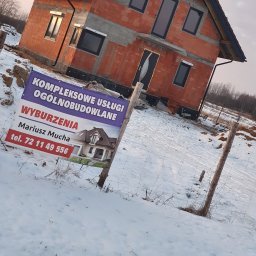 Kompleksowe usługi ogólnobudowlane - Budowa domu z czerwonej cegły w zimowym krajobrazie. Na pierwszym planie baner reklamowy z wizualizacją gotowego budynku i danymi kontaktowymi firmy.