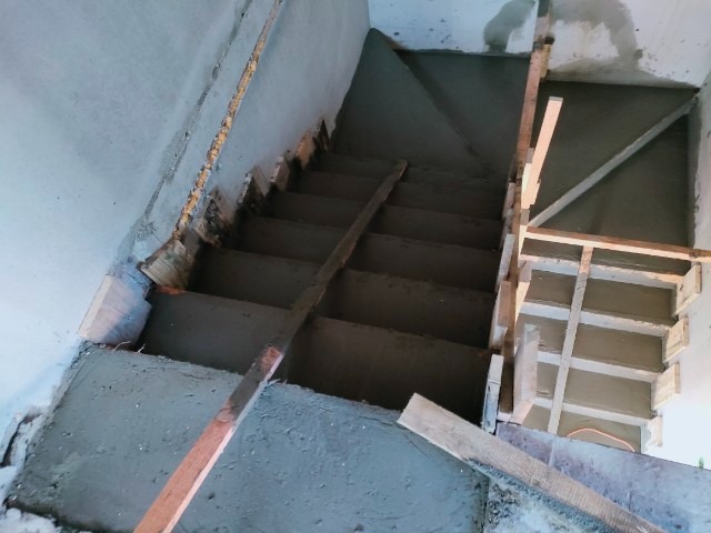 Wylewka betonowa na schodach z drewnianym szalunkiem. Widok z góry na betonowe stopnie w trakcie prac wykończeniowych. Szare ściany i fragmenty drewnianych elementów.