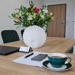 Biuro rachunkowe: drewniany stół z kwiatami, wizytówką, telefonem, długopisem, dokumentem i filiżanką kawy w eleganckim wnętrzu.