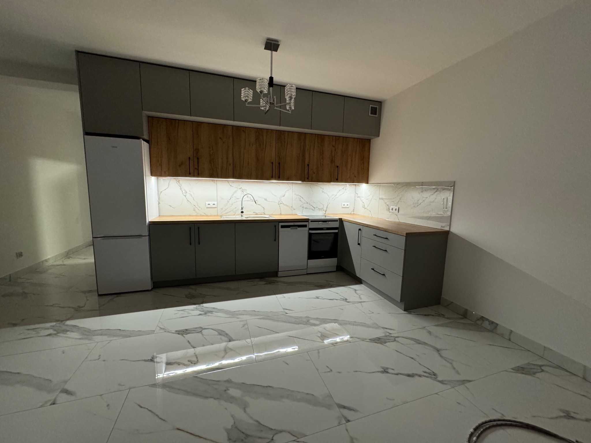 Nowoczesna kuchnia z szarymi i drewnianymi szafkami, marmurową podłogą i designerską lampą wiszącą, widziana z niskiego kąta.