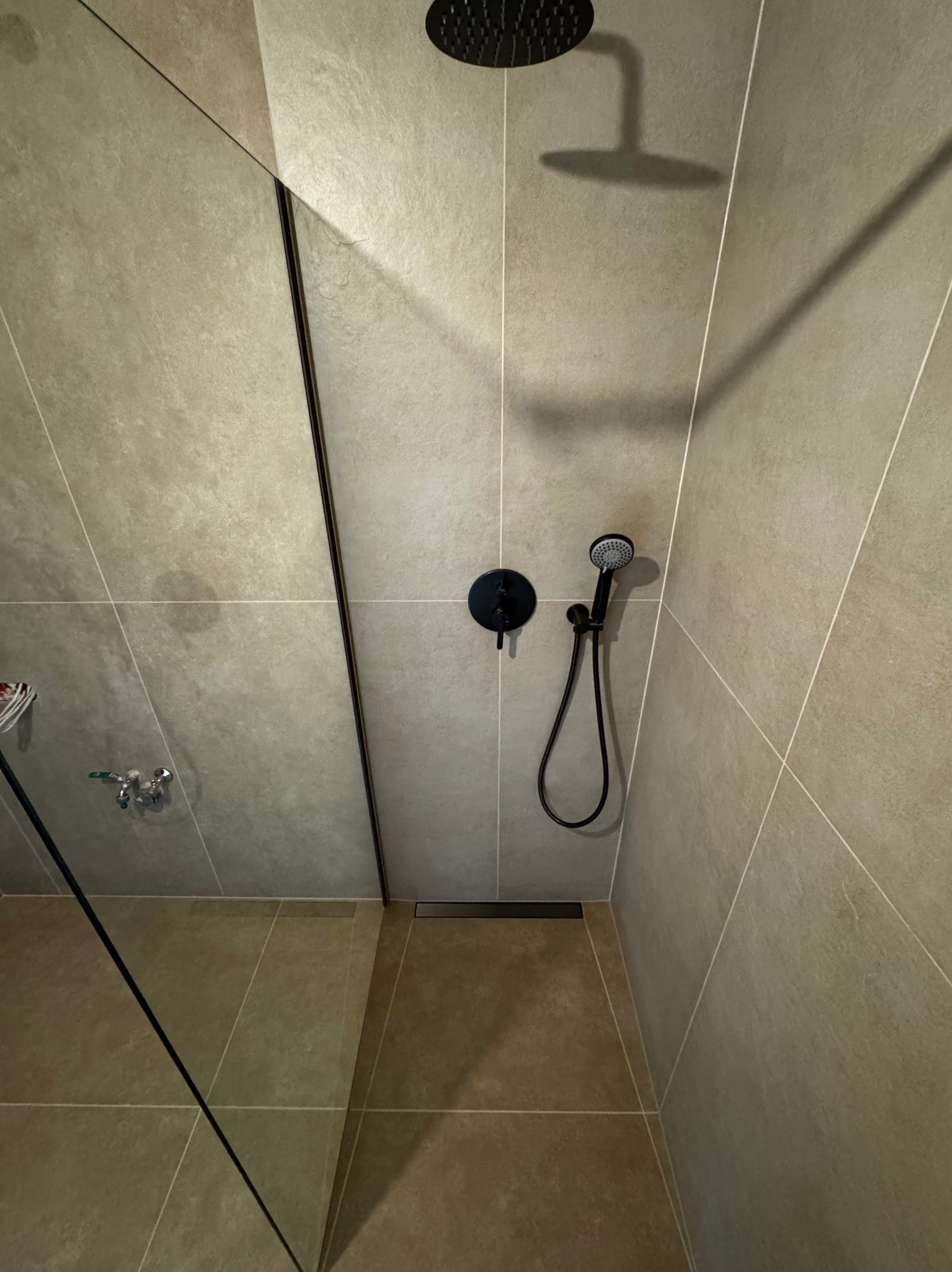 Nowoczesna kabina prysznicowa walk-in z czarną armaturą i odpływem liniowym, wykończona w beżowych płytkach, Marki. Minimalistyczny design i funkcjonalność.