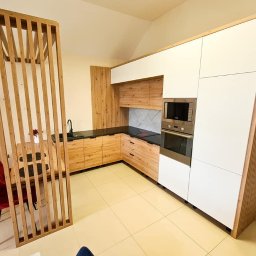 Przedsiębiorstwo Produkcyjno Handlowe ESKA - Jasna kuchnia na wymiar z drewnianymi frontami i białymi szafkami, oddzielona ażurową ścianką od jadalni z czerwonymi krzesłami. Nowoczesne wykończenie.