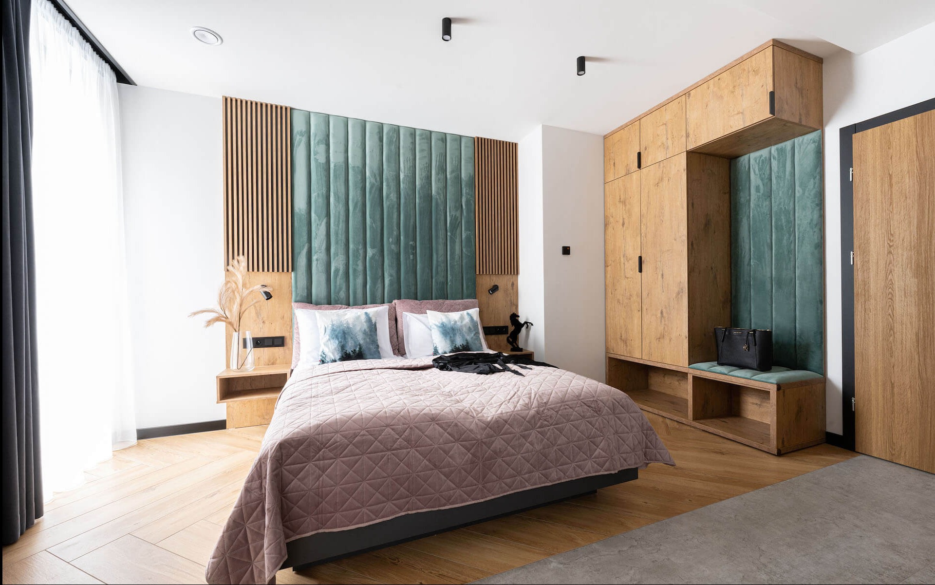 Nowoczesna sypialnia z drewnianą szafą wnękową z siedziskiem obitym zielonym aksamitem, łóżkiem z tapicerowanym zagłówkiem i drewnianymi panelami dekoracyjnymi.