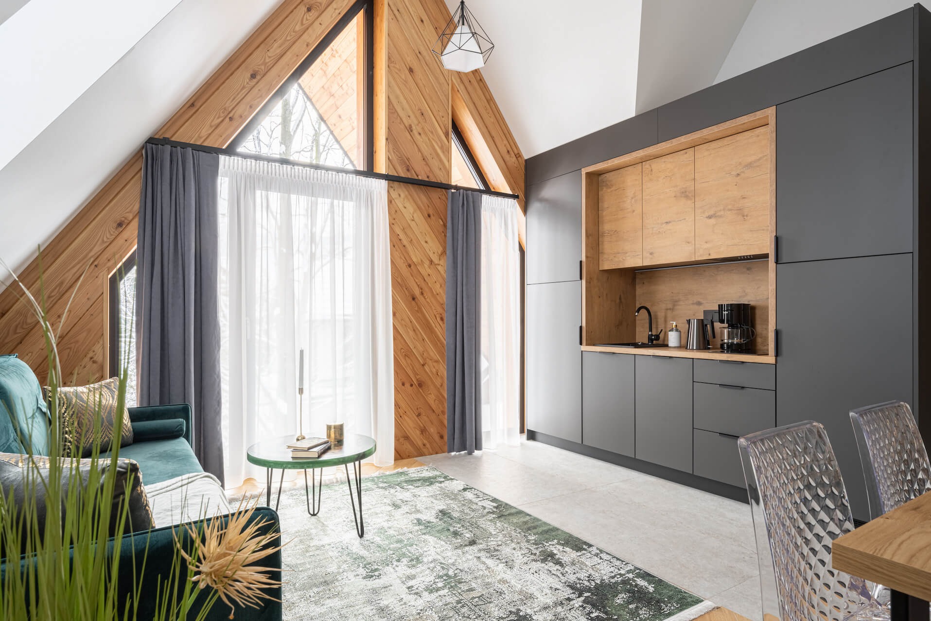 Nowoczesna kuchnia w szarościach i drewnie w Przytkowicach. Zabudowa kuchenna pod skosem dachu, drewniane wykończenie ściany, okno trójkątne, dywan w odcieniach zieleni.