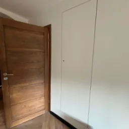 Ukryte drzwi inspekcyjne, zlicowane ze ścianą po wykonaniu prac w Milicz, obok drewniane drzwi wejściowe i parkiet.