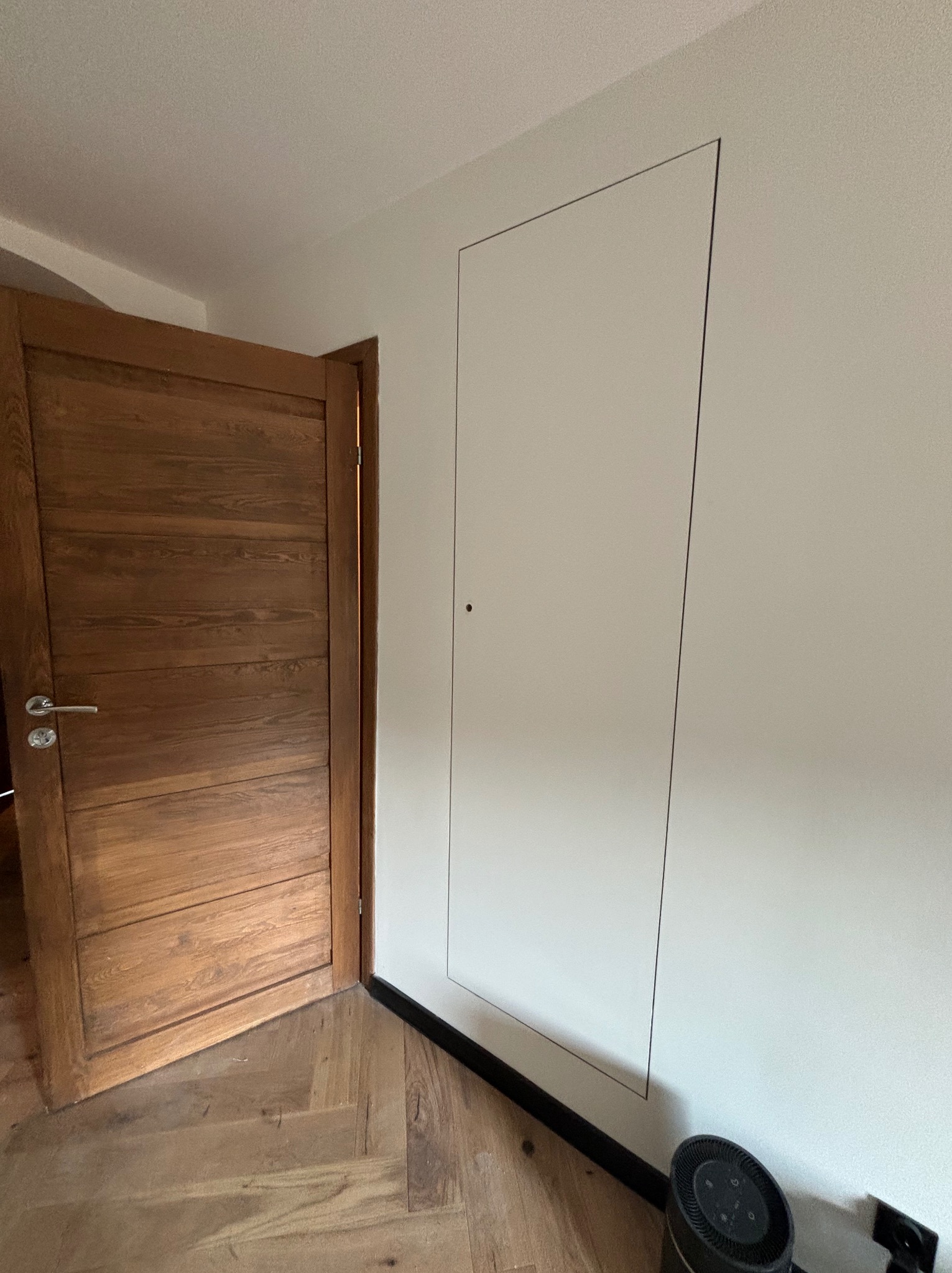 Ukryte drzwi inspekcyjne, zlicowane ze ścianą po wykonaniu prac w Milicz, obok drewniane drzwi wejściowe i parkiet.