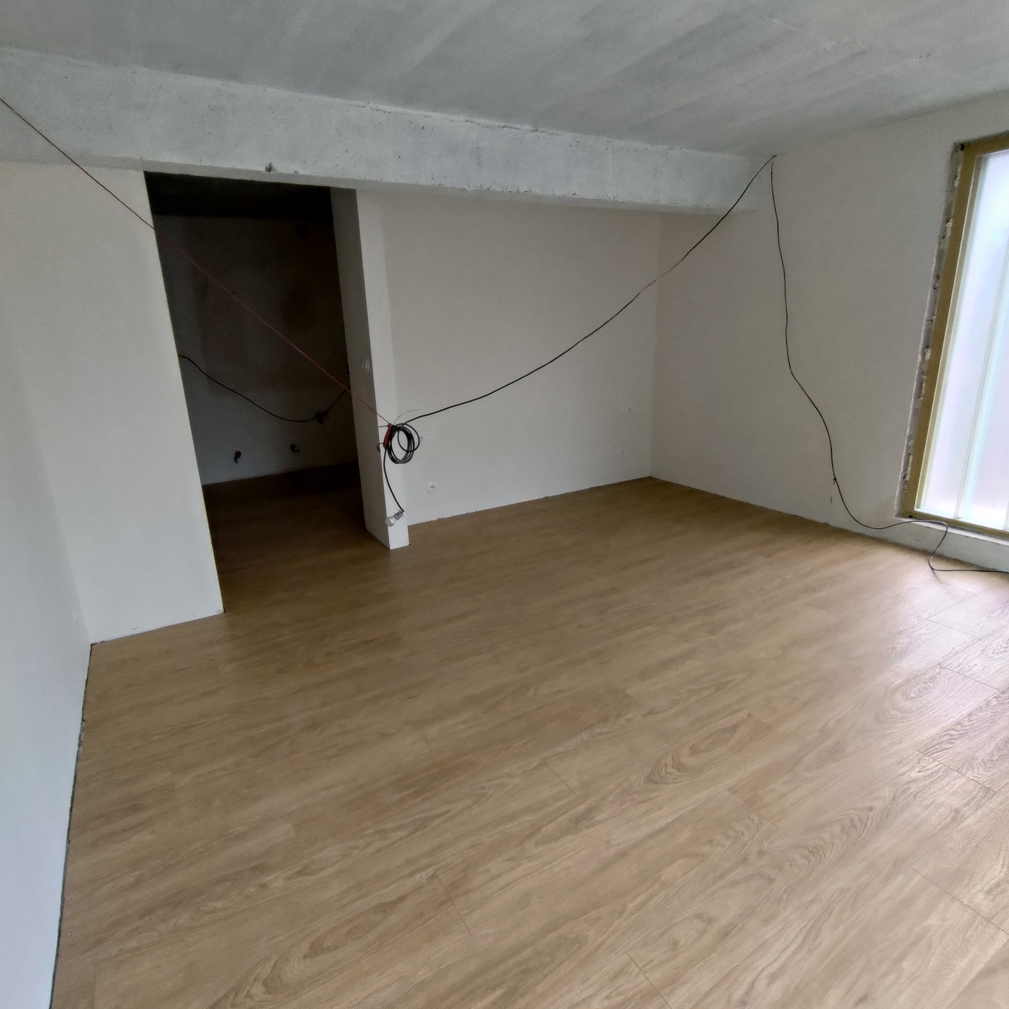 Jasne panele podłogowe w nowym pomieszczeniu z surowym betonowym sufitem i wystającymi kablami.