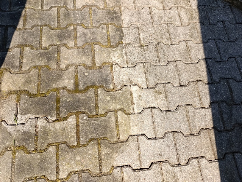 Częściowo oczyszczona kostka brukowa z widocznym kontrastem między brudną, porośniętą mchem powierzchnią a czystą, jasną kostką po zabiegu.