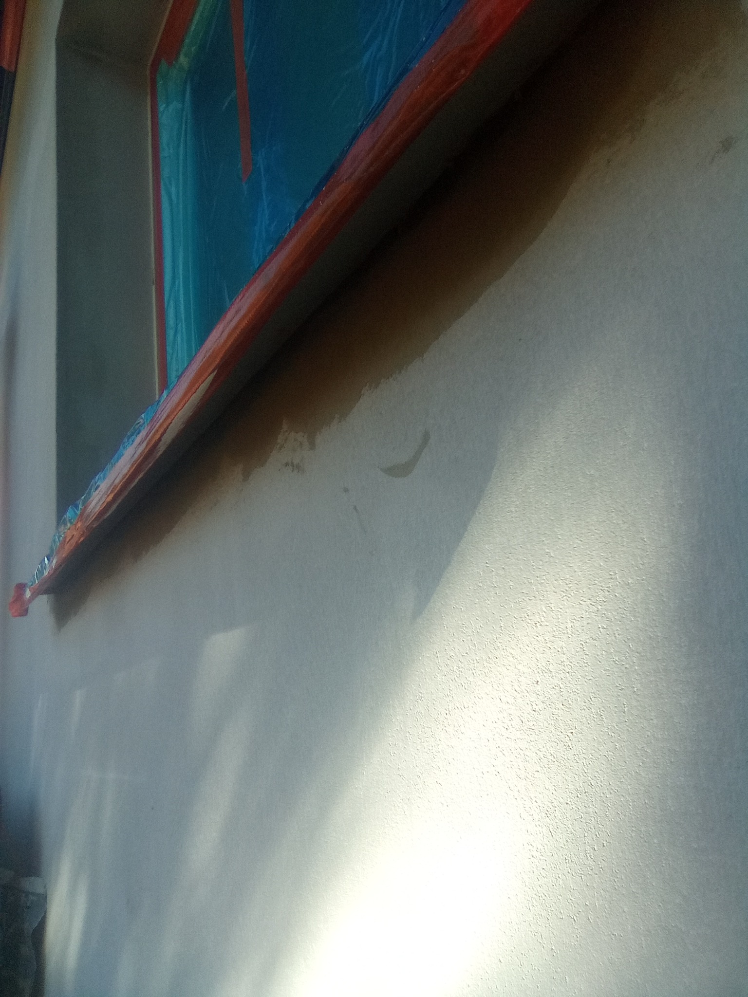 Świeżo otynkowana elewacja z zabezpieczonym oknem folią i taśmą malarską, widoczne delikatne nierówności i cień światła.