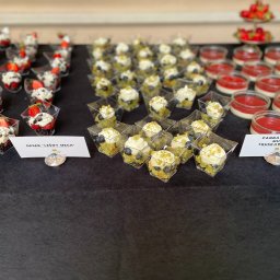 Liv Catering - Desery w małych pojemnikach: leśny mech z borówkami, panna cotta truskawkowa. Elegancki catering deserowy na czarnym obrusie, z bliska.