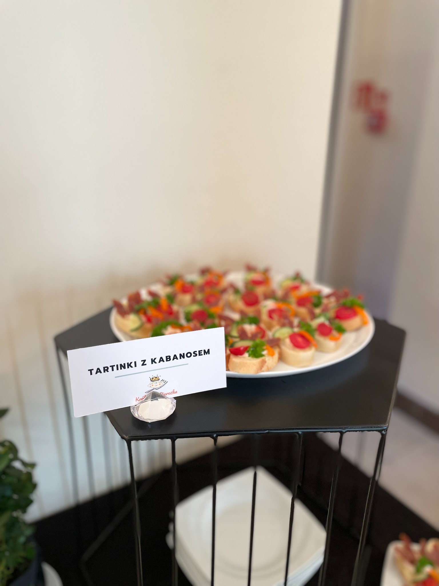 Tarty z kabanosem na białym talerzu, ustawione na czarnym stoliku. Obok widoczna kartka z napisem 'Tartinki z kabanosem'.