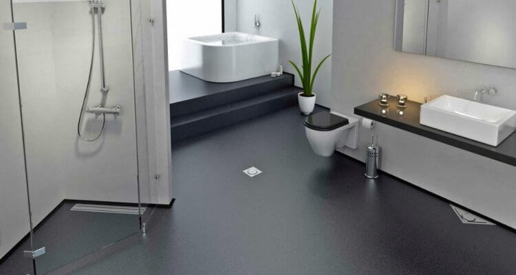 Nowoczesna łazienka z ciemną, jednolitą posadzką żywiczną, kabiną prysznicową ze szklaną ścianą, wanną i umywalką na blacie. Minimalistyczny design, jasne ściany.