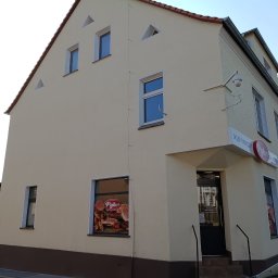 Max Global - Jasna elewacja budynku sklepu z brązowym pasem u dołu. Widoczne okna, drzwi wejściowe i szyld sklepu. Ujęcie z dołu, podkreślające wysokość budynku.