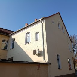Max Global - Odnowiona elewacja budynku z klimatyzatorem, widoczna z perspektywy ulicy w słoneczny dzień. Jasna, gładka fasada kontrastuje z sąsiednim budynkiem o starszej elewacji.