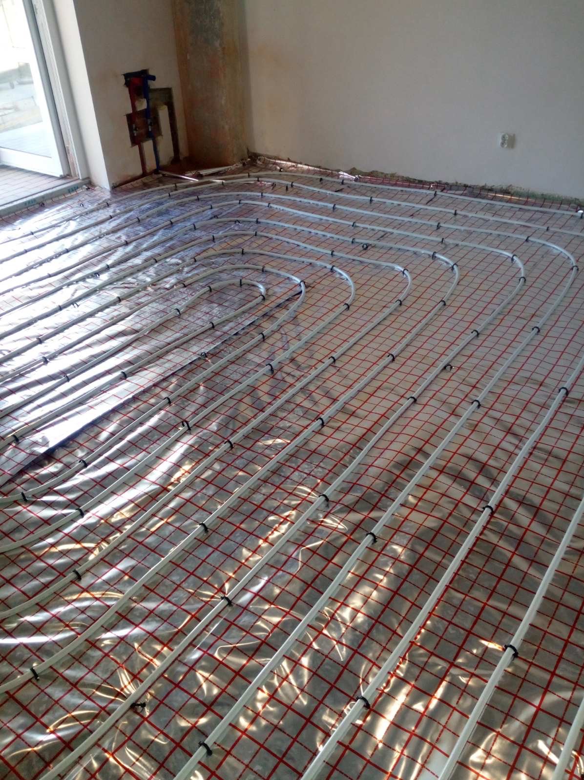 Rozłożone rury ogrzewania podłogowego na folii izolacyjnej z siatką w nowym pomieszczeniu przed wylewką.