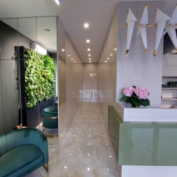 TIK Tomasz Górecki - Nowoczesne wnętrze z zielonymi akcentami: pionowa ściana z roślin, welurowe fotele z złotymi nogami, designerska lampa w kształcie ptaków i lśniąca posadzka.