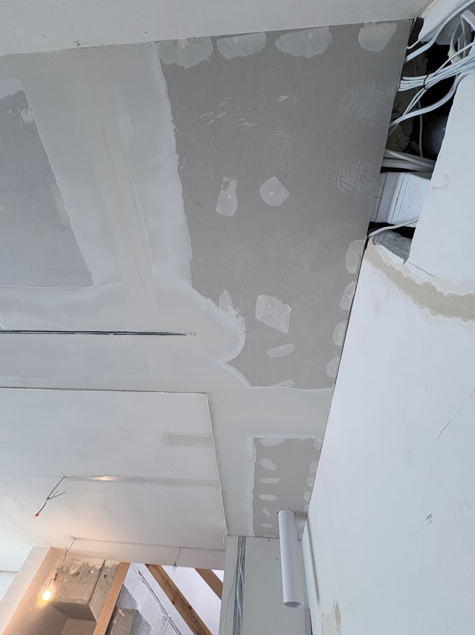 Sufit z płyt kartonowo-gipsowych w trakcie szpachlowania, widoczne kable i instalacje. Ujęcie z dołu, sufit częściowo wykończony, widoczne łączenia płyt.