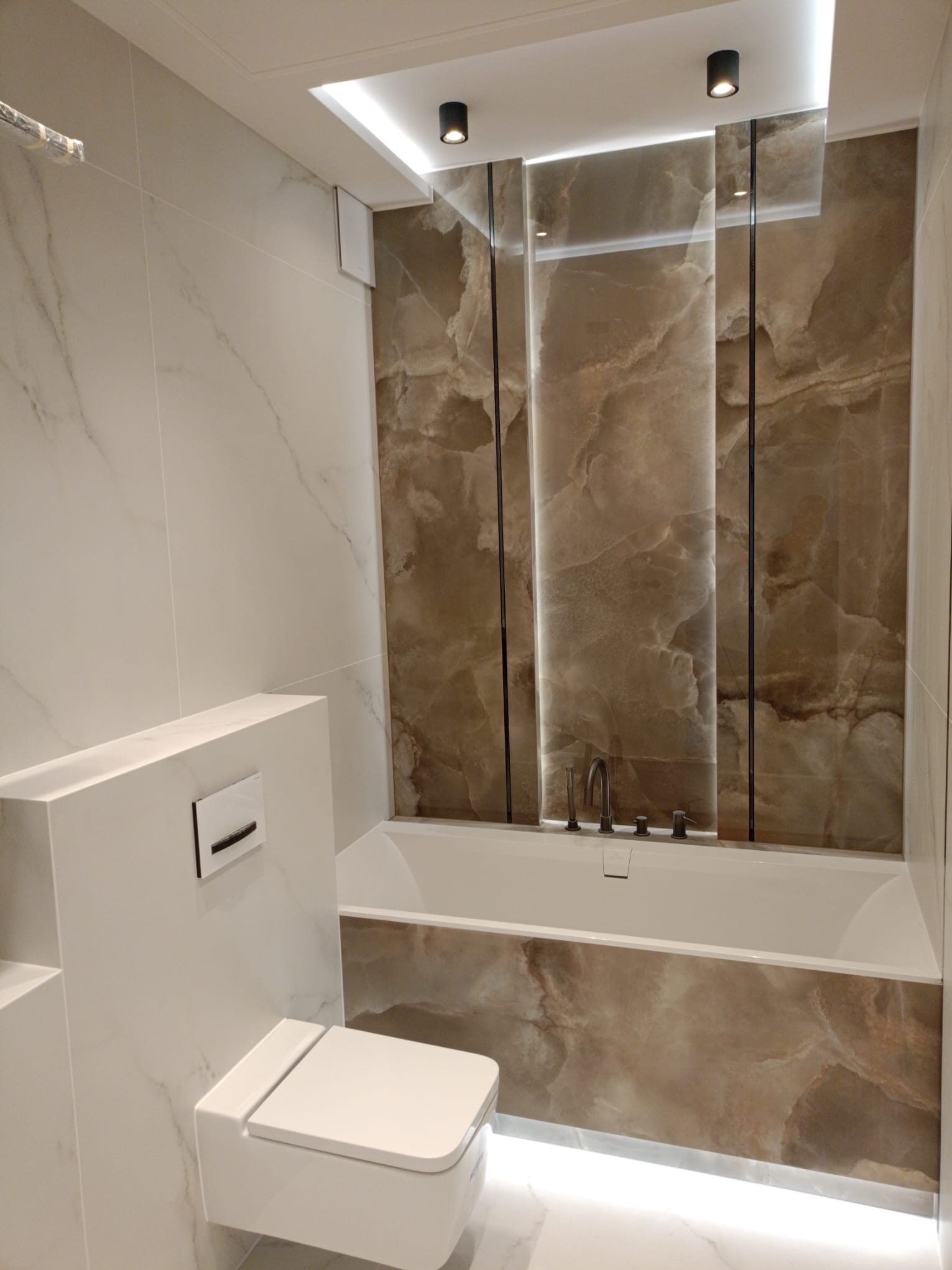 Wykończona łazienka z wanną i podwieszaną toaletą w Siechnicach. Płytki imitujące marmur, podświetlenie LED i minimalistyczna armatura tworzą elegancki wystrój.