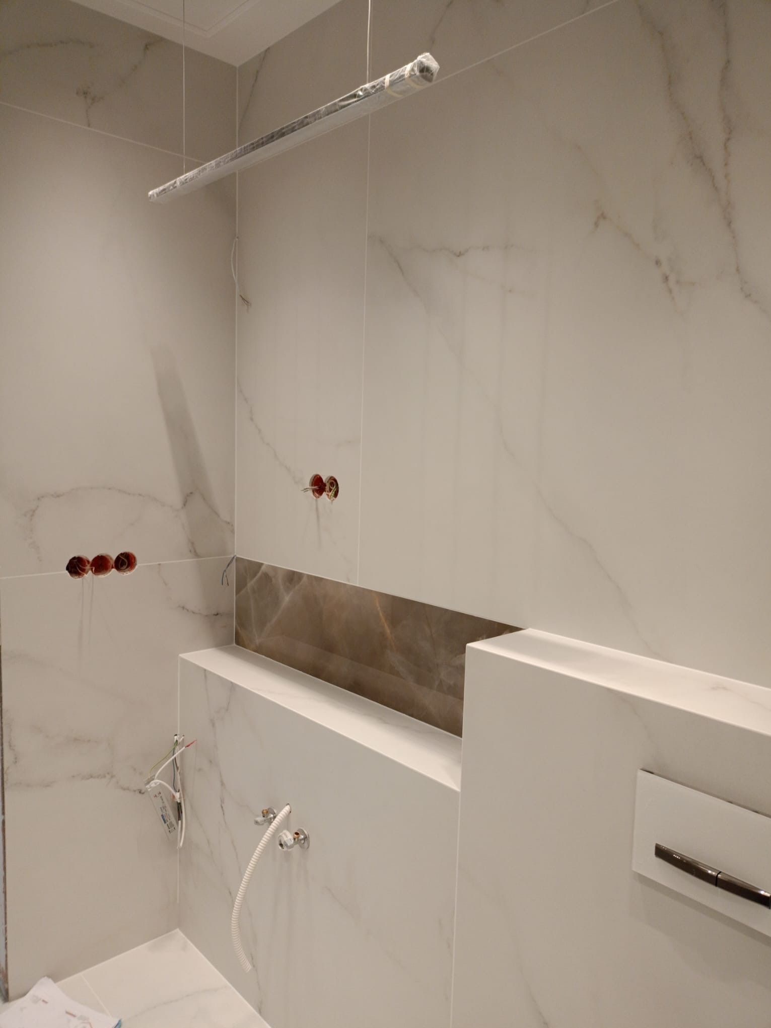 Elegancka łazienka w trakcie wykańczania: marmurowe płytki, podwieszana armatura, widoczne instalacje elektryczne i hydrauliczne. Minimalistyczny design.