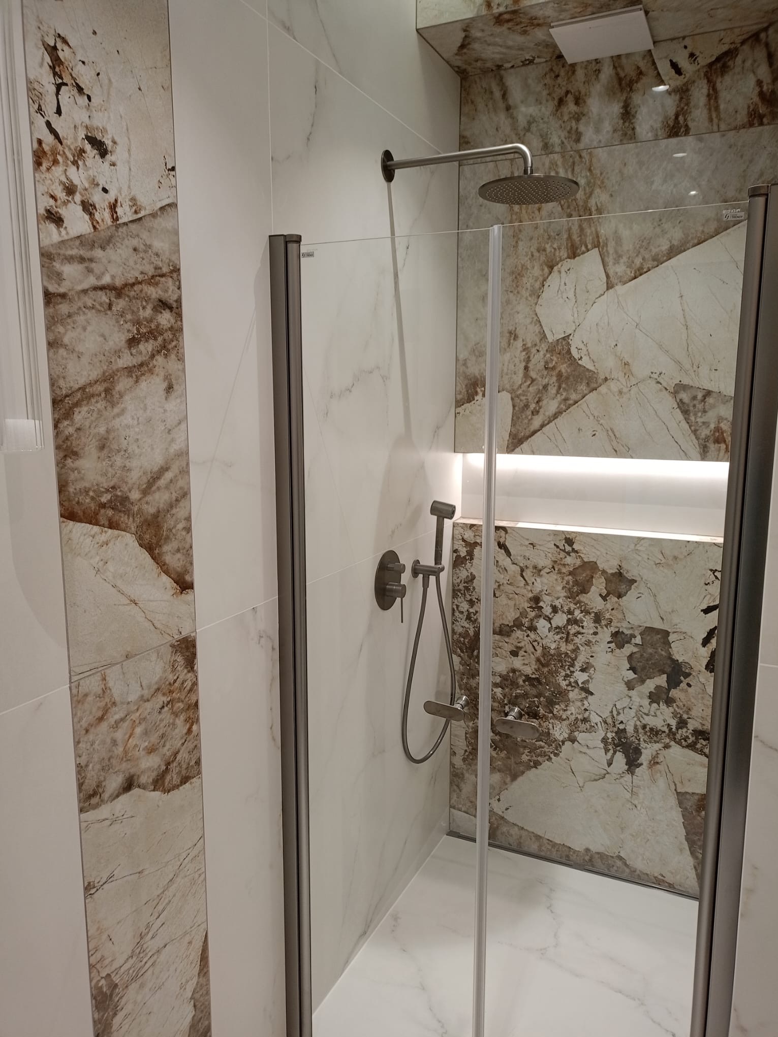 Nowoczesna kabina prysznicowa z deszczownicą i marmurowymi płytkami w odcieniach bieli i brązu. Podświetlana wnęka dodaje elegancji. Minimalistyczny design.