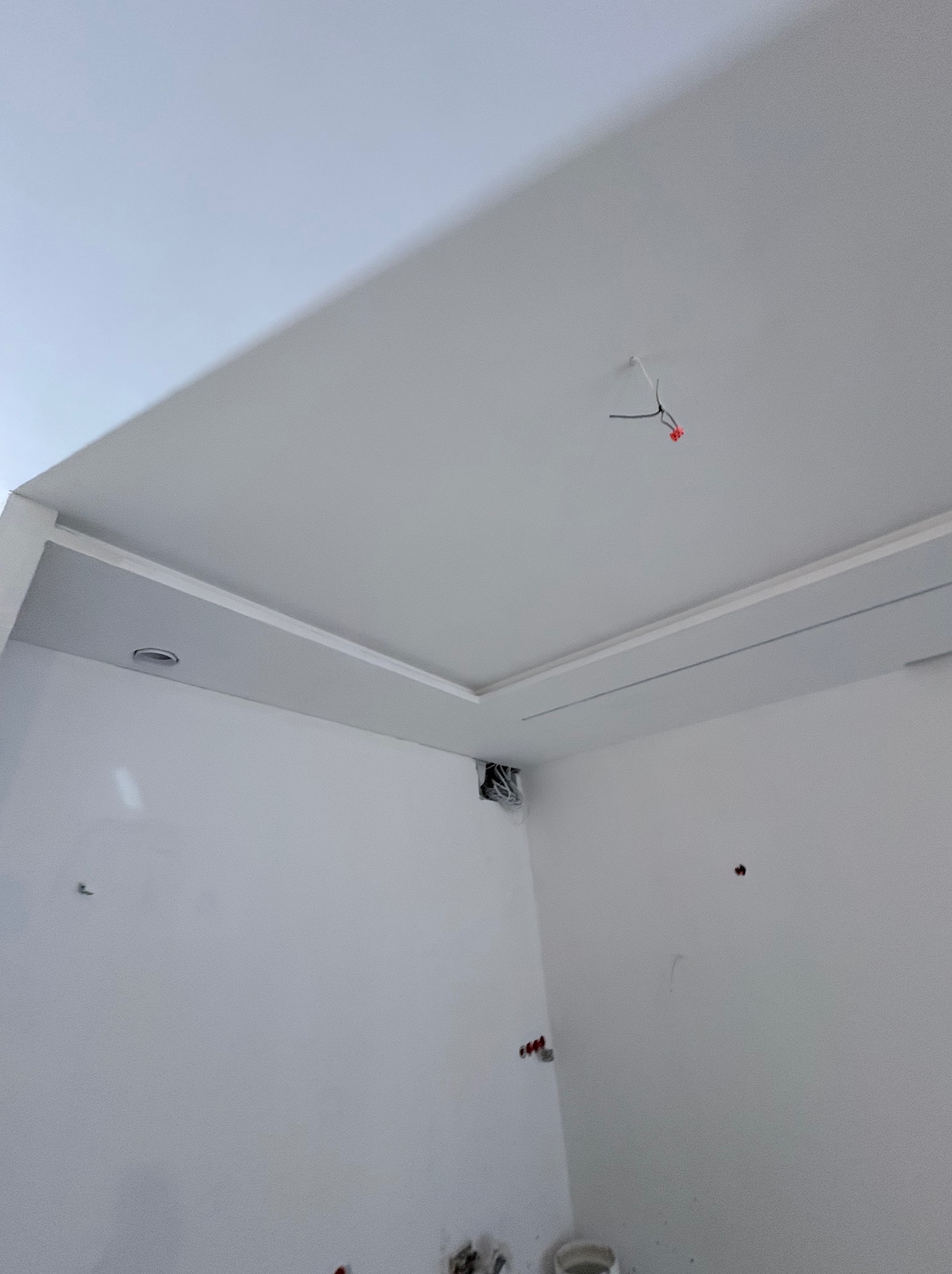 Białe wnętrze po remoncie: gładkie ściany, sufit z dekoracyjnym obniżeniem i punktowe oświetlenie. Widoczne przewody elektryczne.