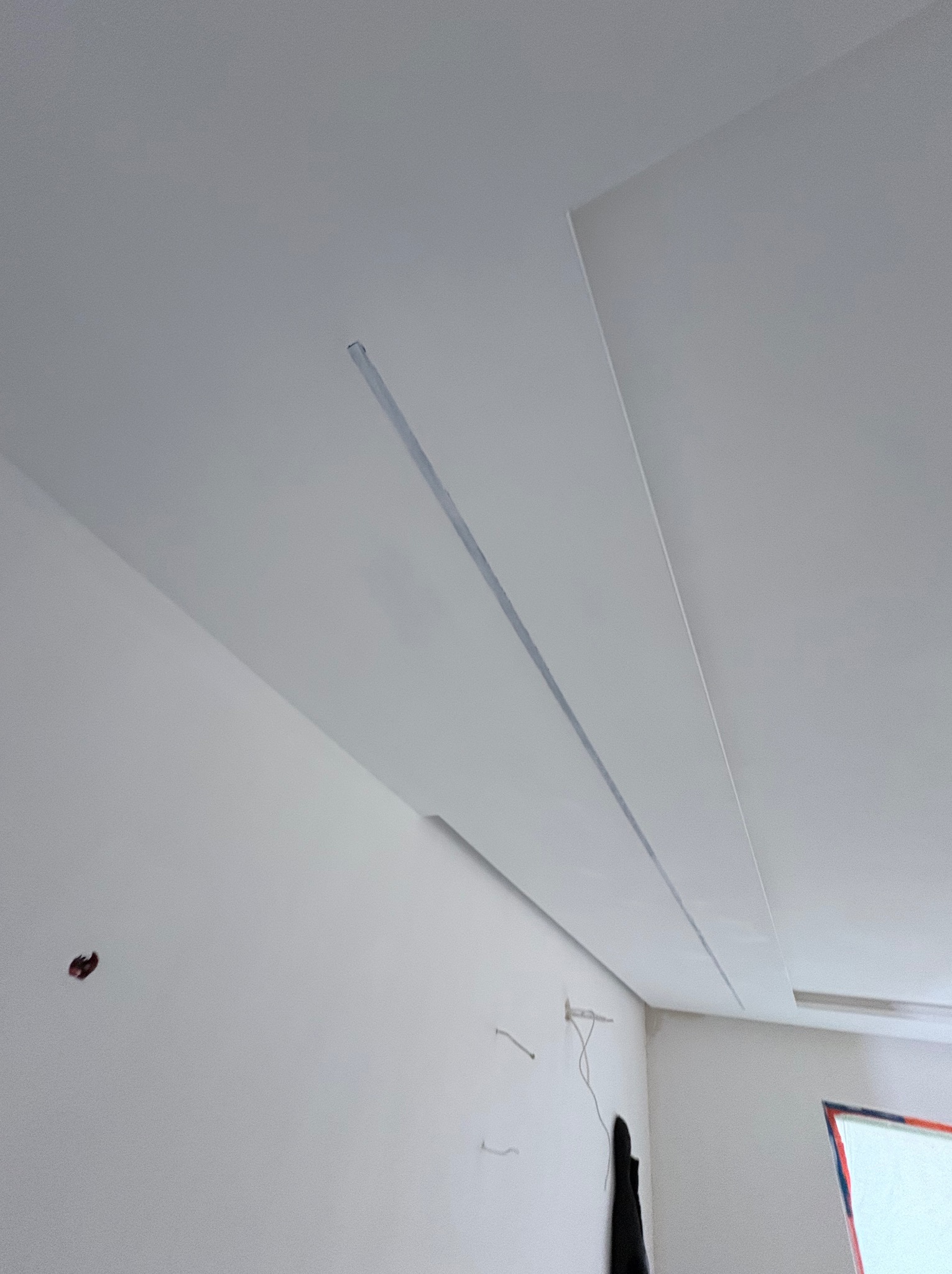 Biały sufit podwieszany z oświetleniem liniowym w trakcie montażu. Widoczne niedoskonałości na ścianie i wystające przewody. Minimalistyczny design.