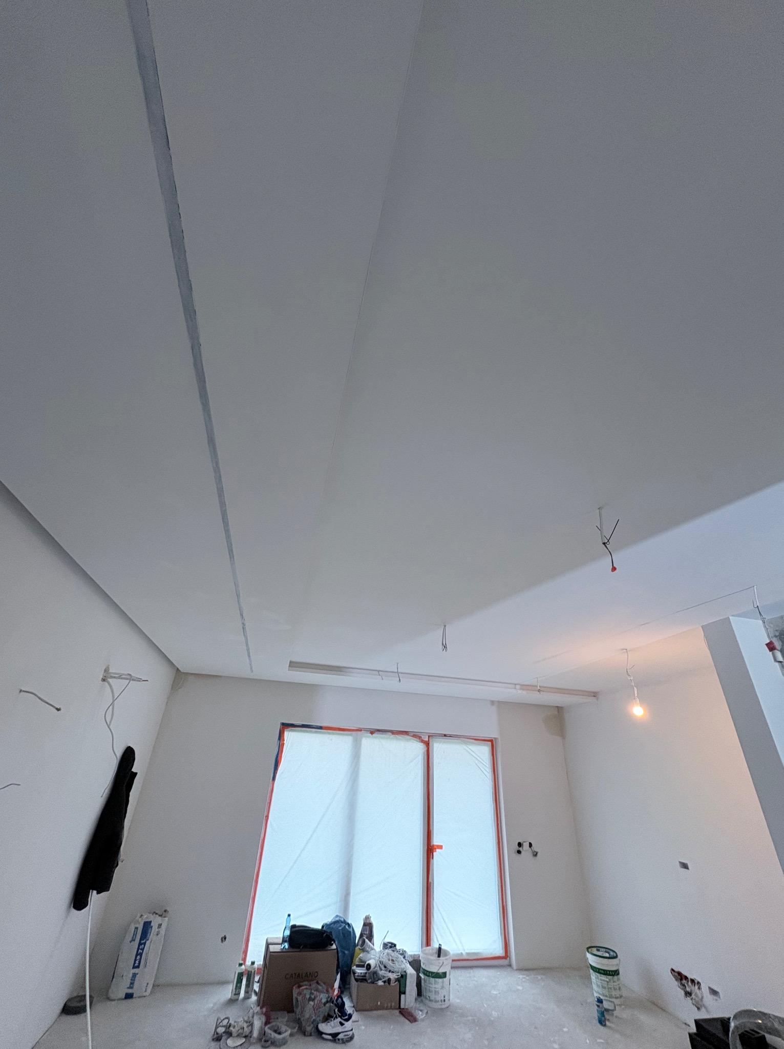 Białe, wykończone sufity podwieszane z widocznymi łączeniami w jasnym wnętrzu w trakcie prac wykończeniowych. Widoczne narzędzia i materiały budowlane.