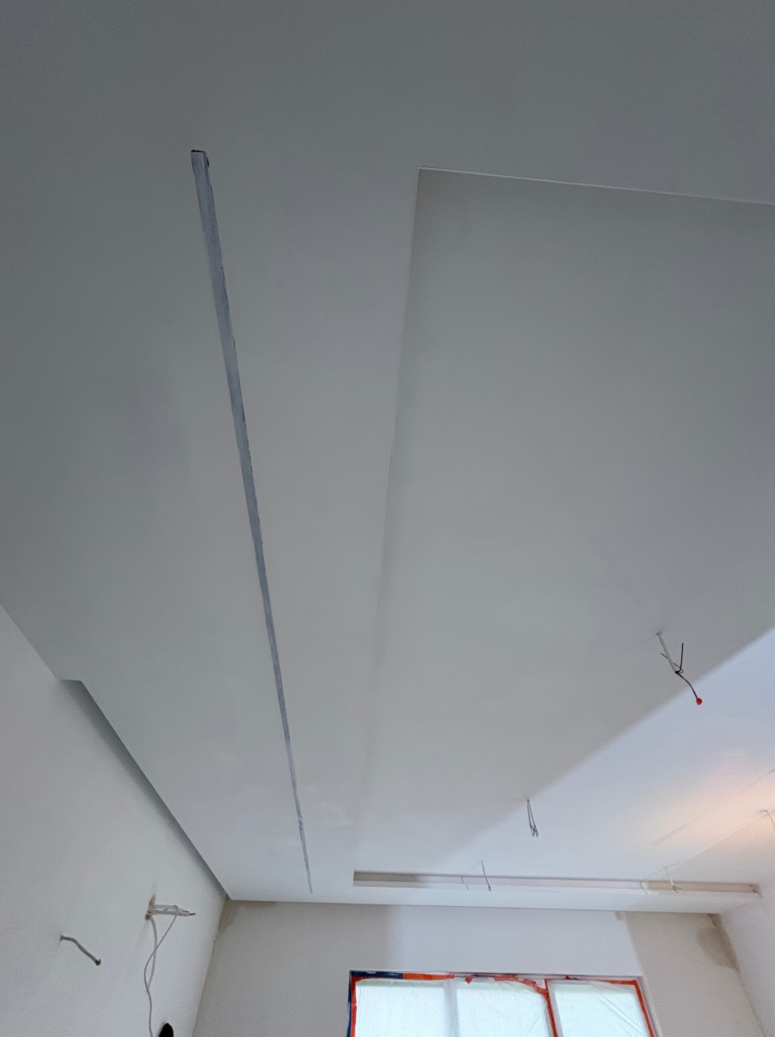 Sufit podwieszany z widocznymi liniami podziału, świeżo po montażu, z elementami instalacji elektrycznej. Okno zabezpieczone folią malarską.