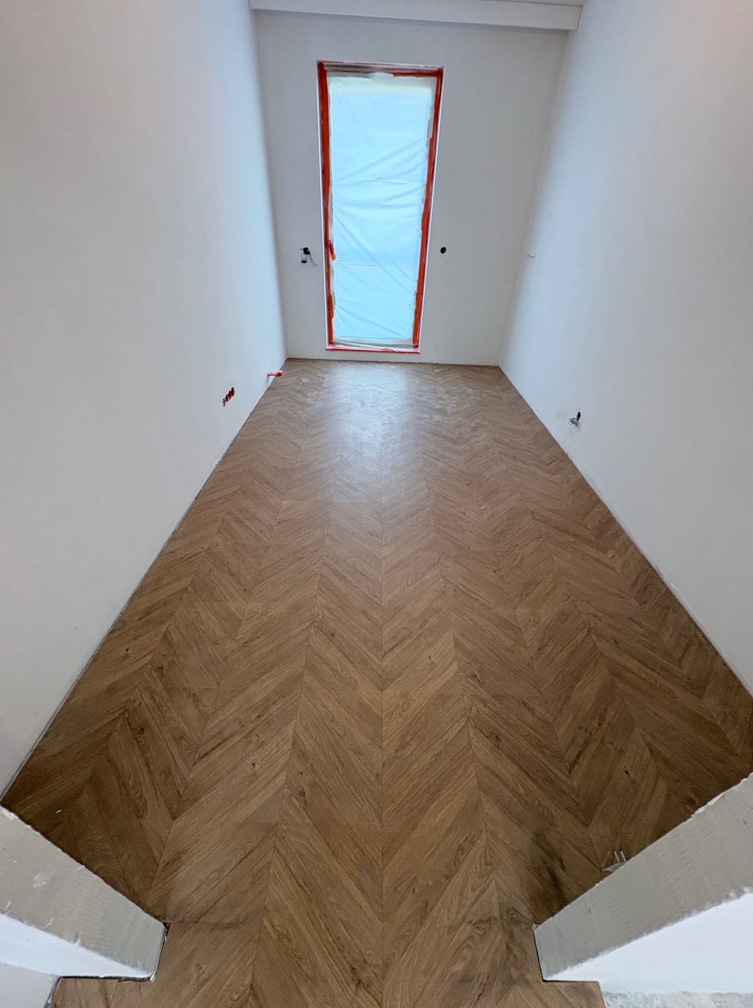 Ukończone układanie parkietu w jodełkę francuską w jasnym pomieszczeniu z oknem dachowym zabezpieczonym folią. Widok z dołu, świeżo po realizacji.