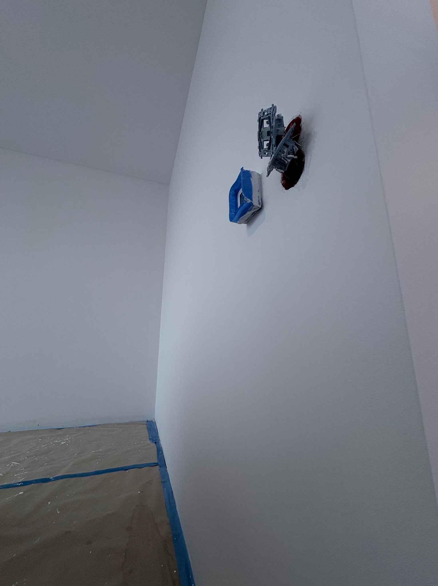 Biała ściana z zabezpieczonym gniazdkiem elektrycznym taśmą malarską. Podłoga zabezpieczona folią malarską. Przygotowanie do malowania.