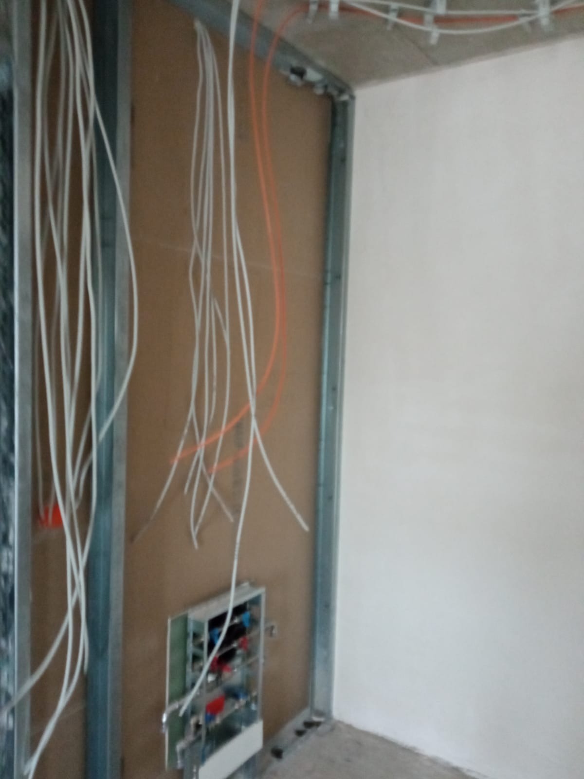 Niedokończona instalacja elektryczna w nowym budynku, widoczne kable wystające ze ściany i metalowa rama konstrukcyjna.
