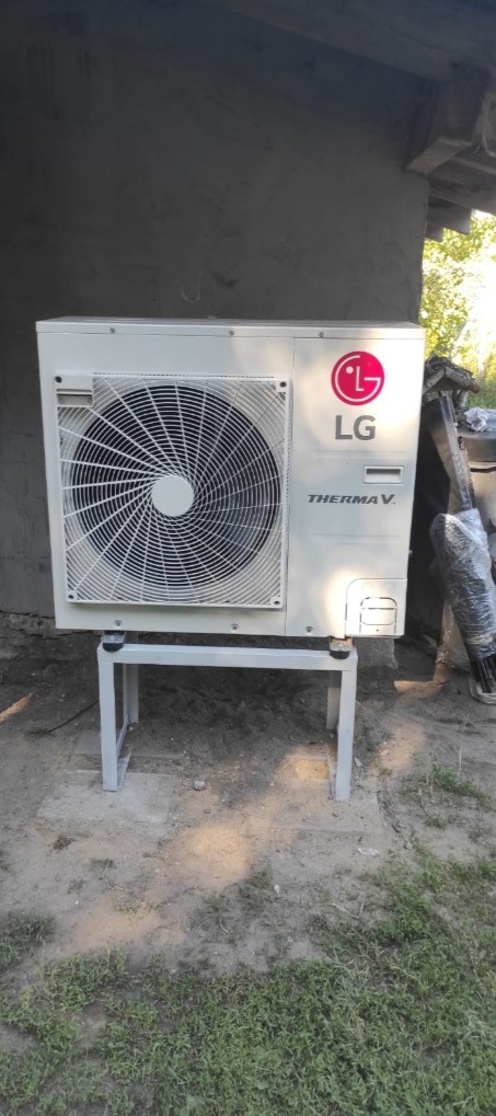 Zewnętrzna jednostka pompy ciepła LG Therma V zamontowana na metalowym stelażu, na zewnątrz budynku, z widocznym logo LG i wentylatorem.