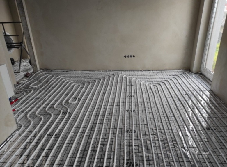 Rozłożone rury ogrzewania podłogowego na siatce montażowej w surowym pomieszczeniu przed wylewką.