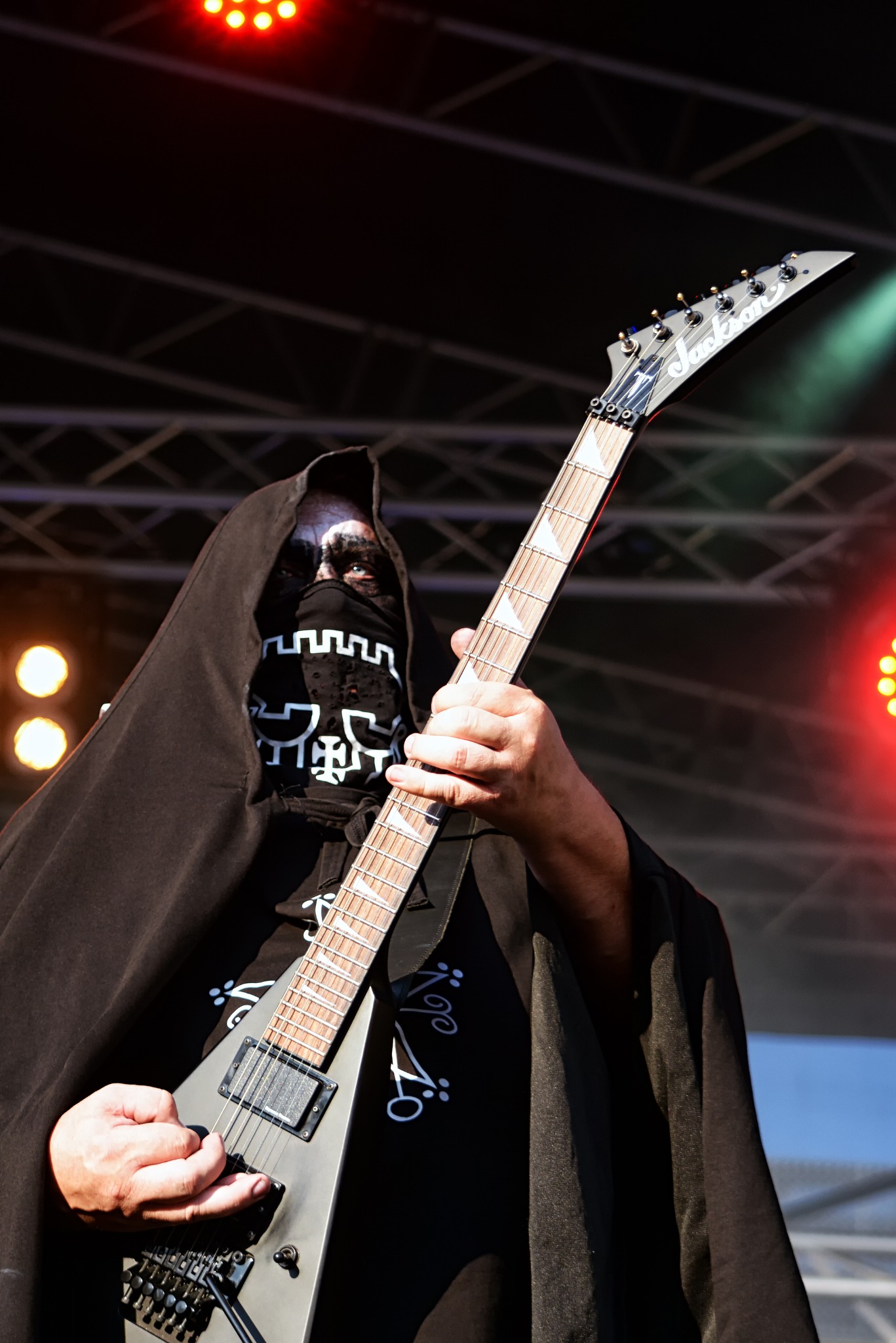 Gitarzysta w kapturze i masce na scenie koncertowej, trzymający gitarę Jackson. W tle oświetlenie sceniczne i konstrukcja kratowa. MetalMine 2024.