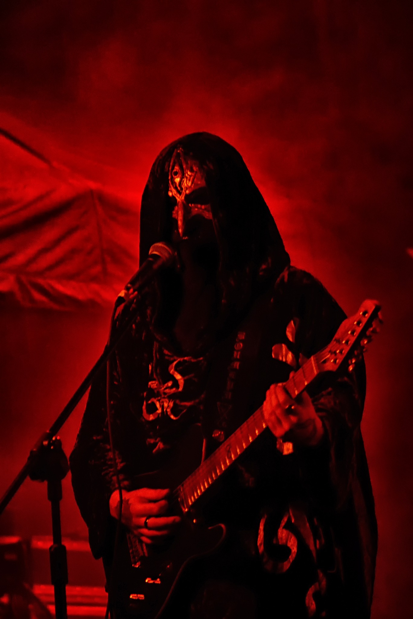 Mroczna fotografia koncertowa z Wrocławia: gitarzysta w kapturze i masce, oświetlony czerwonym światłem podczas występu na MetalMine 2024.