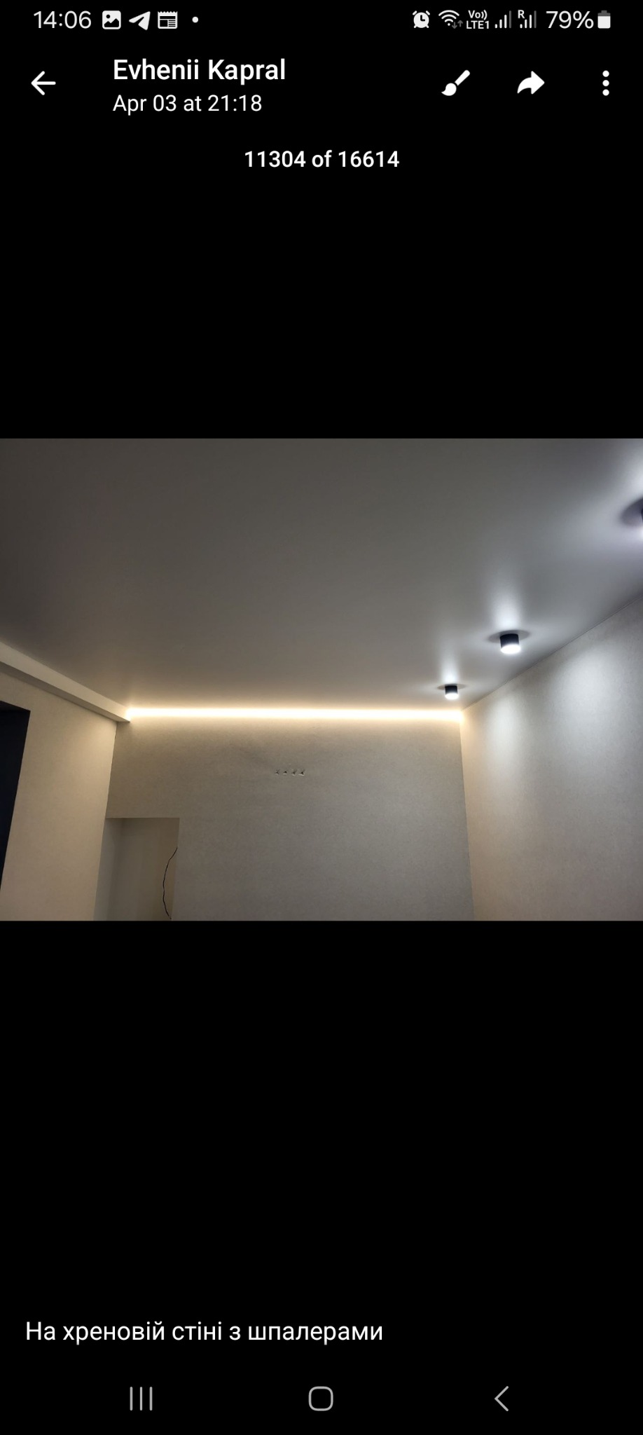 Nowoczesne wnętrze z podwieszonym sufitem z oświetleniem LED, minimalistyczne czarne lampy sufitowe, ściany o delikatnej fakturze i widoczny fragment wnęki w ścianie.