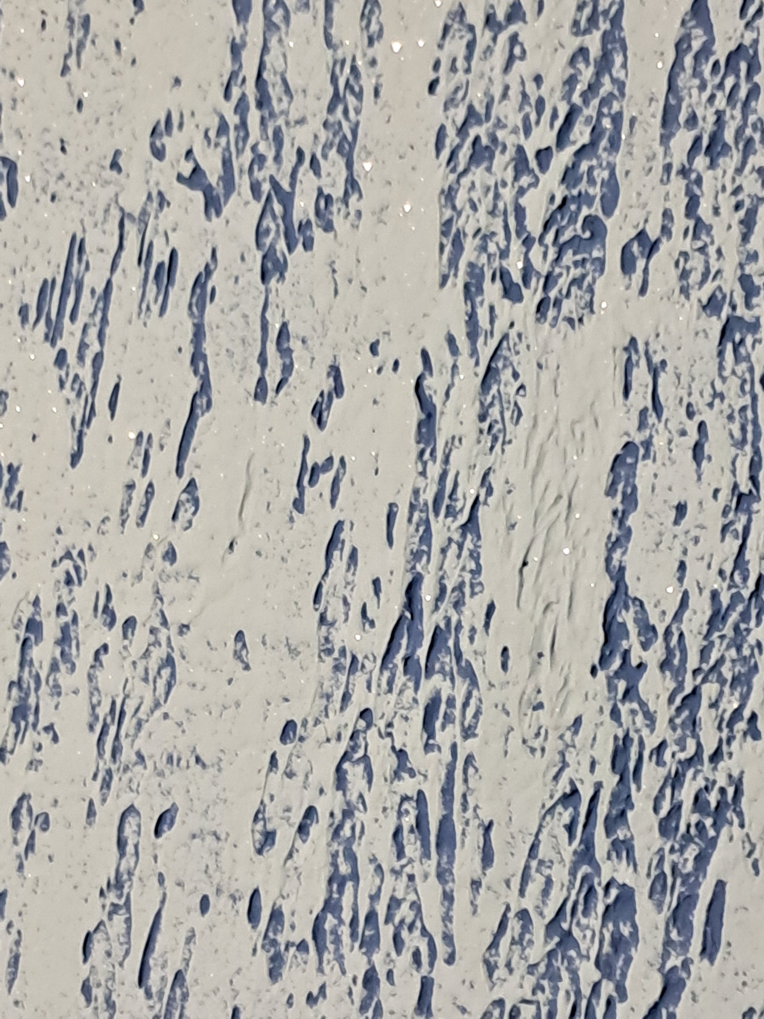 Biała, strukturalna ściana z widocznymi, nieregularnymi wgłębieniami w odcieniach niebieskiego, tworzącymi efekt trójwymiarowości.