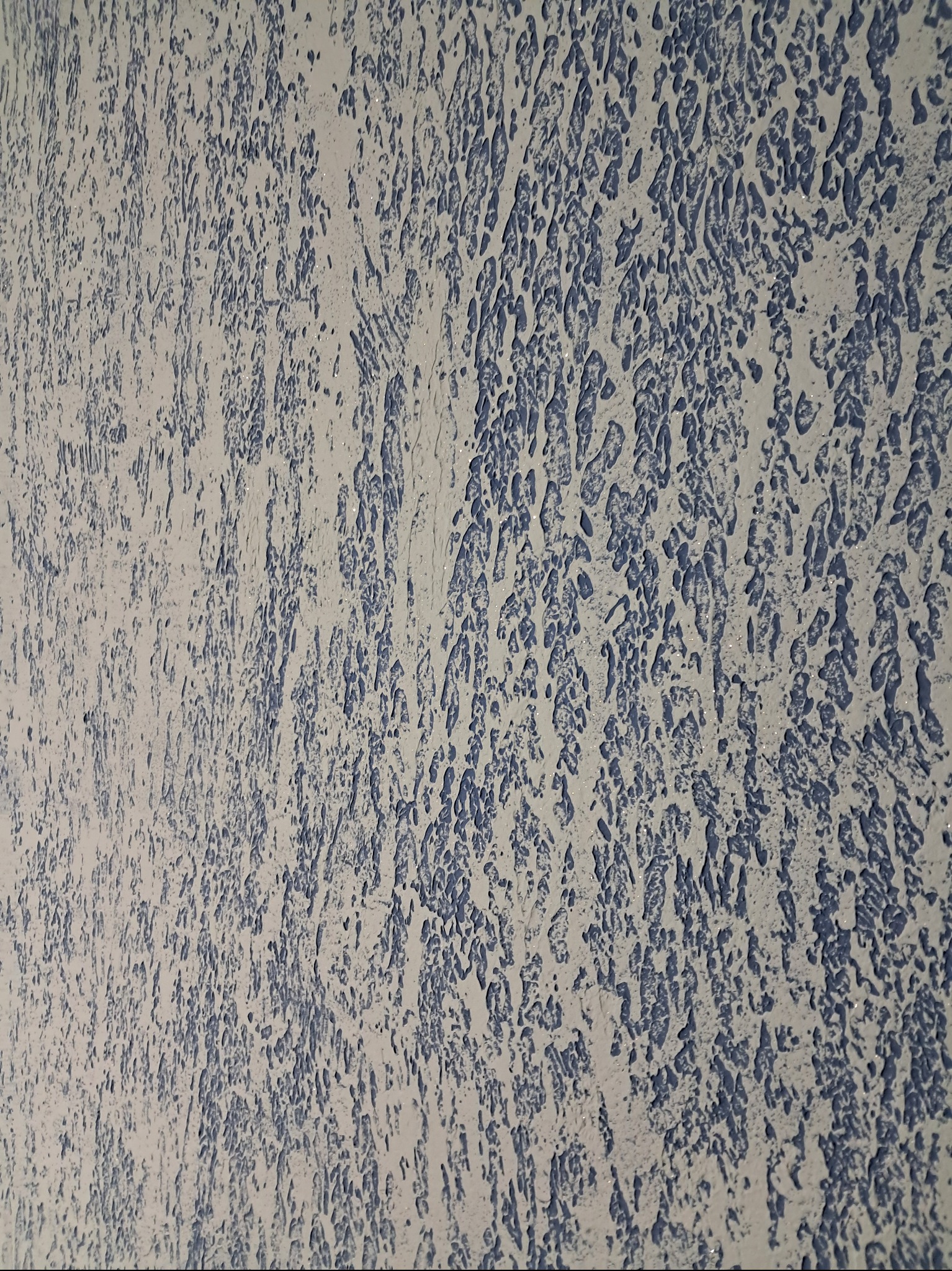 Szpachlowana ściana z dekoracyjną fakturą w odcieniach bieli i błękitu, imitująca efekt naturalnego kamienia.