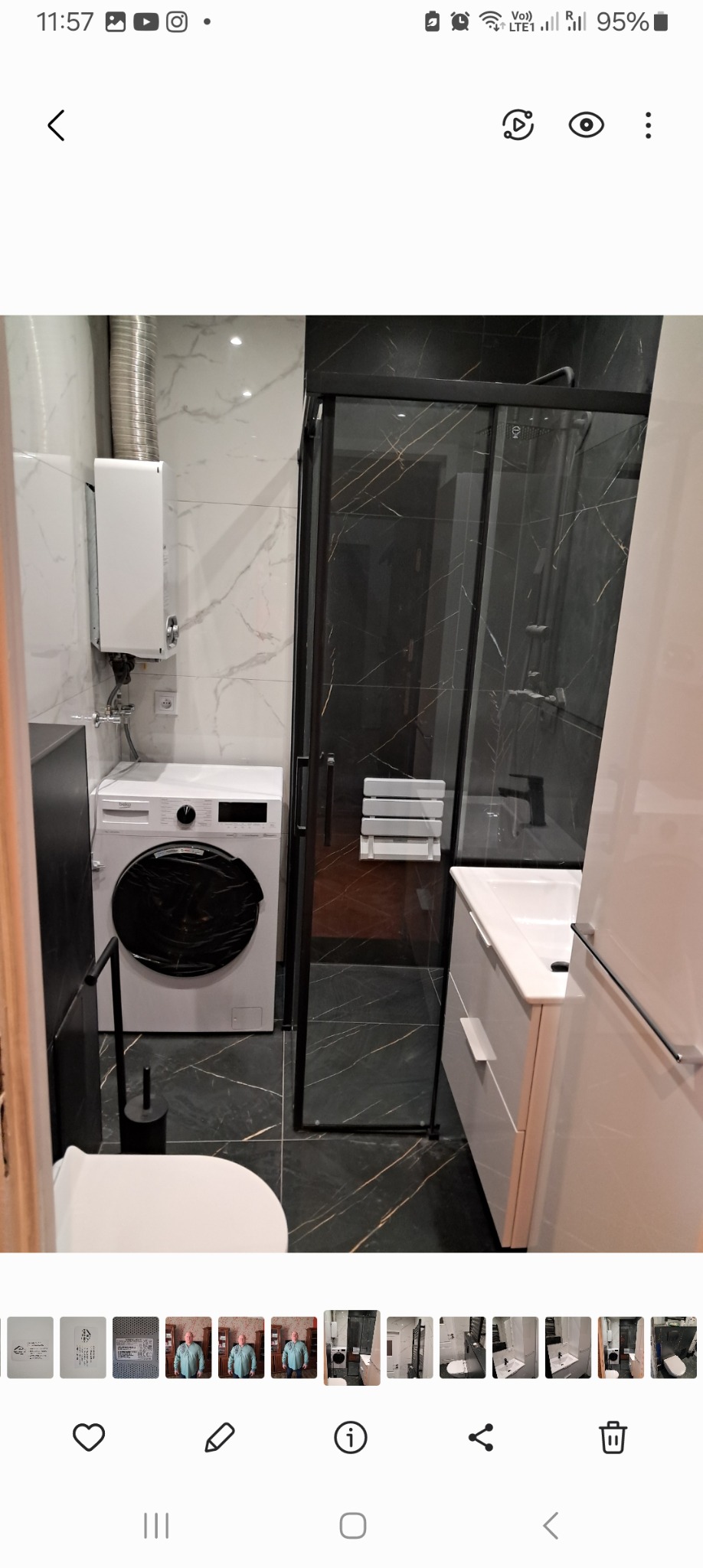 Nowoczesna łazienka z czarną kabiną prysznicową z marmurowym wzorem, białą pralką i wiszącym bojlerem, wykończona białymi i czarnymi płytkami imitującymi marmur.