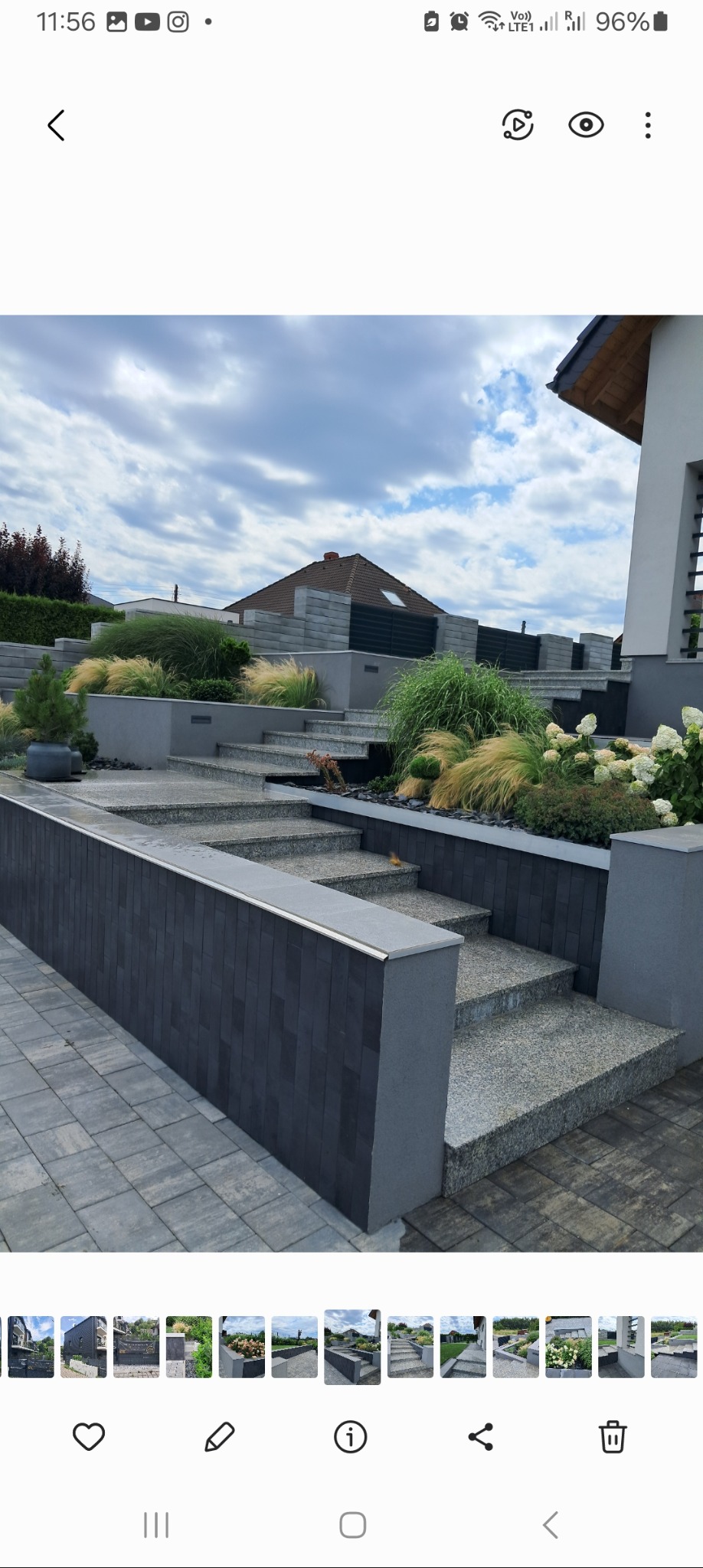 Schody zewnętrzne z szarego granitu prowadzące do domu, otoczone roślinnością ozdobną, w tym trawami i hortensjami, z ciemnoszarymi elementami murków i kostki brukowej.