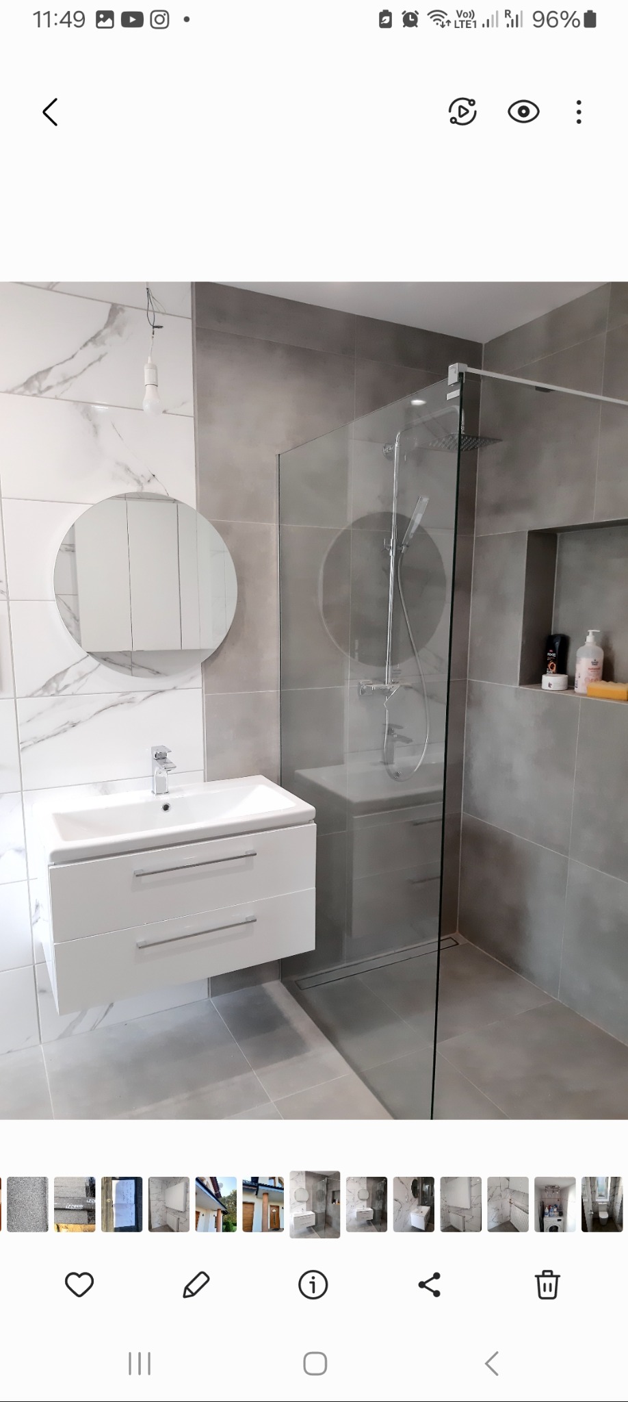 Nowoczesna łazienka z kabiną prysznicową typu walk-in, umywalką z szafką wiszącą i okrągłym lustrem, wykończona płytkami w odcieniach szarości i bieli z marmurkowym wzorem.