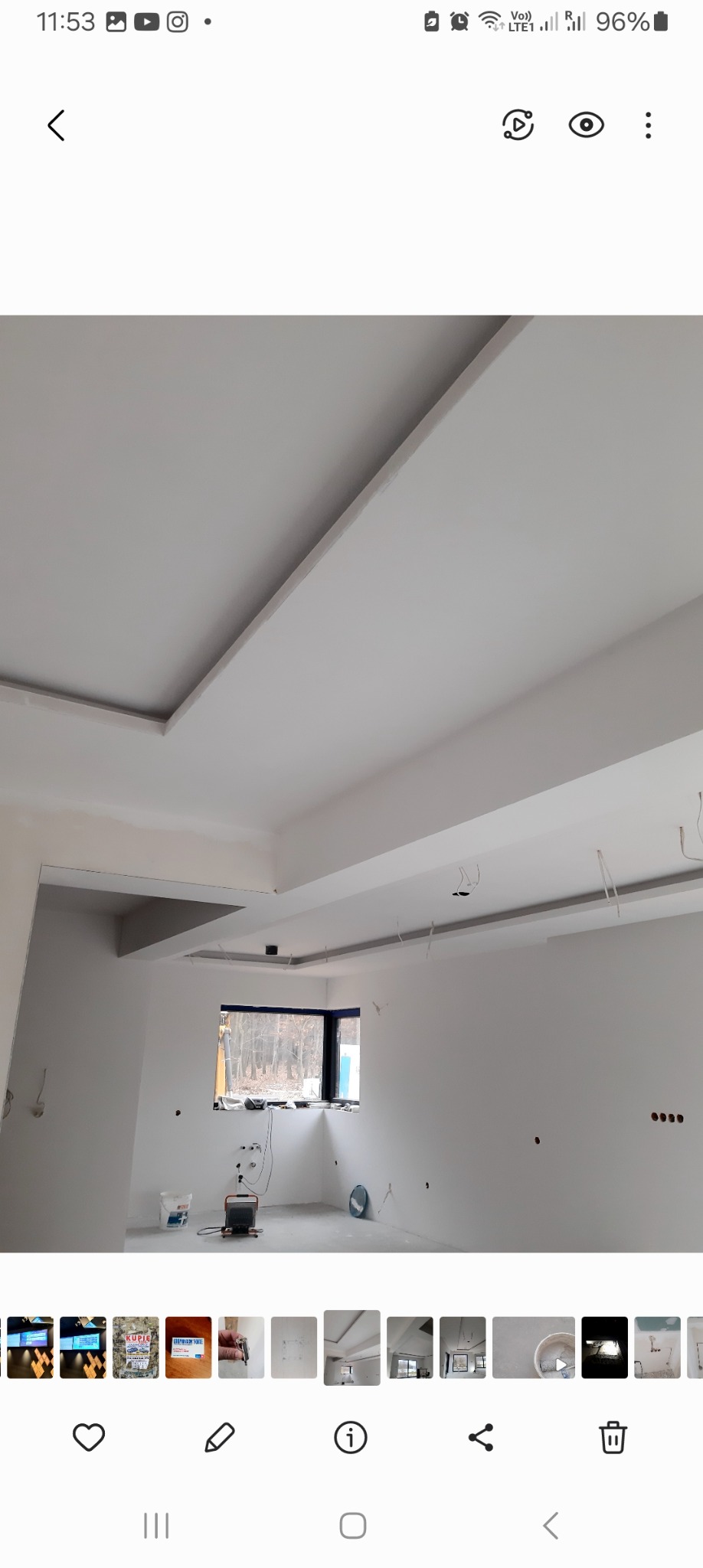 Wykończony sufit z płyt kartonowo-gipsowych z dekoracyjnymi wgłębieniami i wnękami, widoczne przygotowane otwory na oświetlenie, surowy stan ścian i podłogi w pomieszczeniu z oknem.