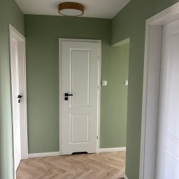 RIKO GROUP SPÓŁKA Z OGRANICZONĄ ODPOWIEDZIALNOŚCIĄ - Korytarz po remoncie: zielone ściany, białe drzwi z czarnymi klamkami i parkiet ułożony w jodełkę. Widoczne dwa okrągłe plafony.