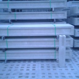 Dax - Stos prefabrykowanych elementów ogrodzeniowych z otworami, zabezpieczonych zielonym sznurkiem, na betonowej nawierzchni.