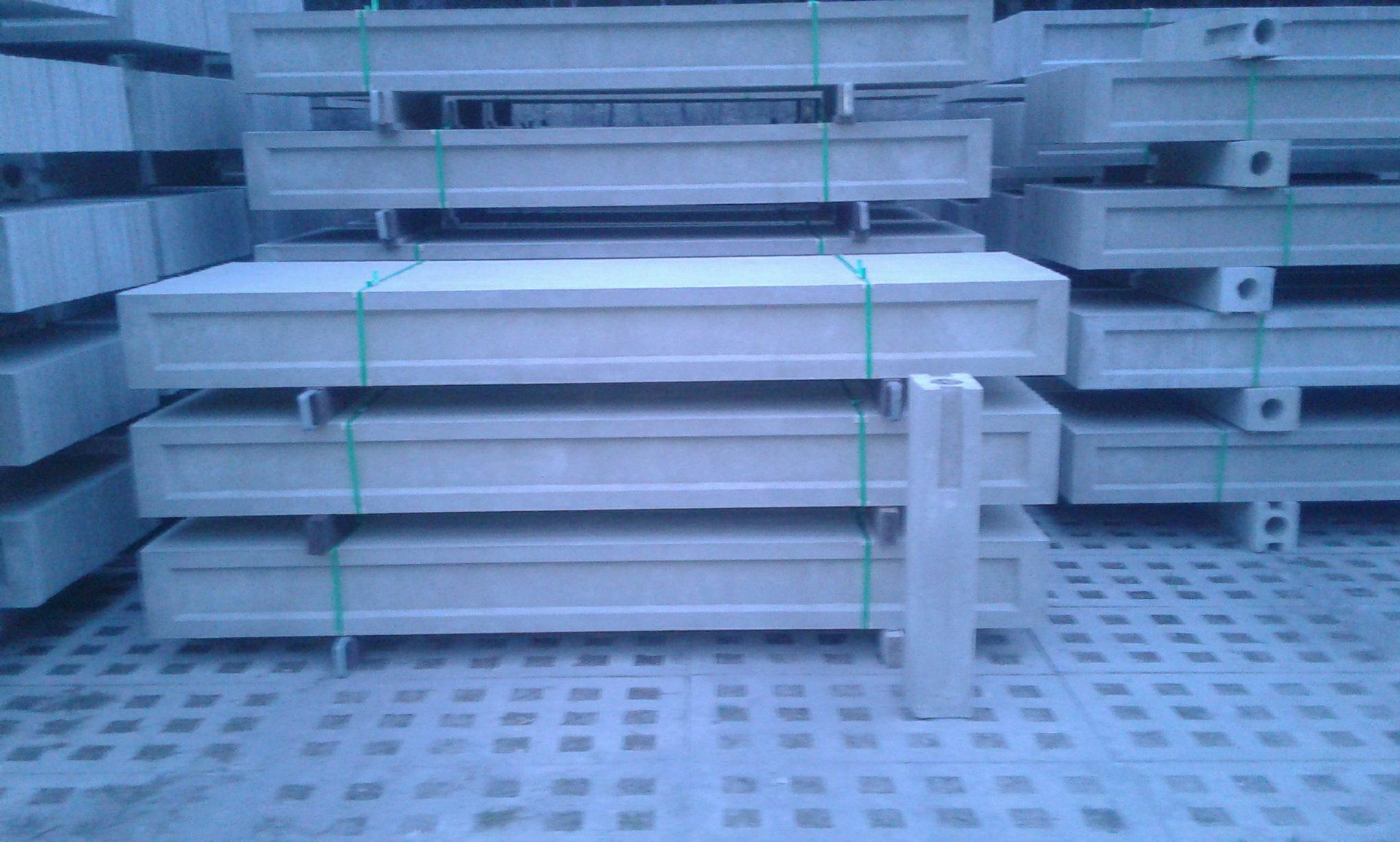 Stos prefabrykowanych elementów ogrodzeniowych z otworami, zabezpieczonych zielonym sznurkiem, na betonowej nawierzchni.