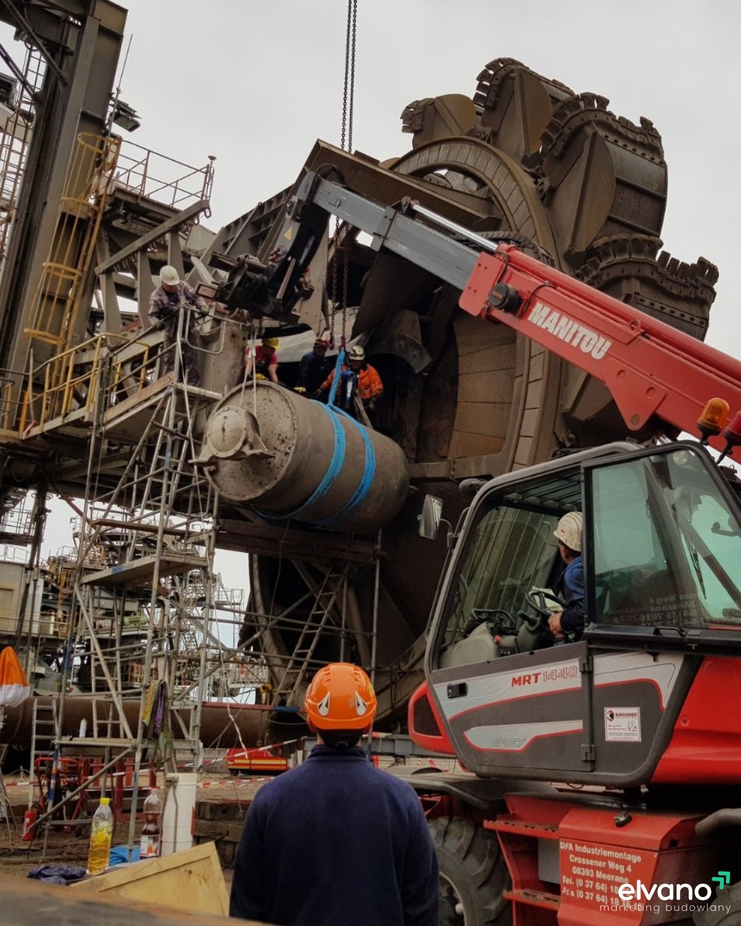 Montaż lub naprawa gigantycznej maszyny przemysłowej z użyciem podnośnika Manitou i rusztowań, pracownicy w kaskach zabezpieczają element linami.