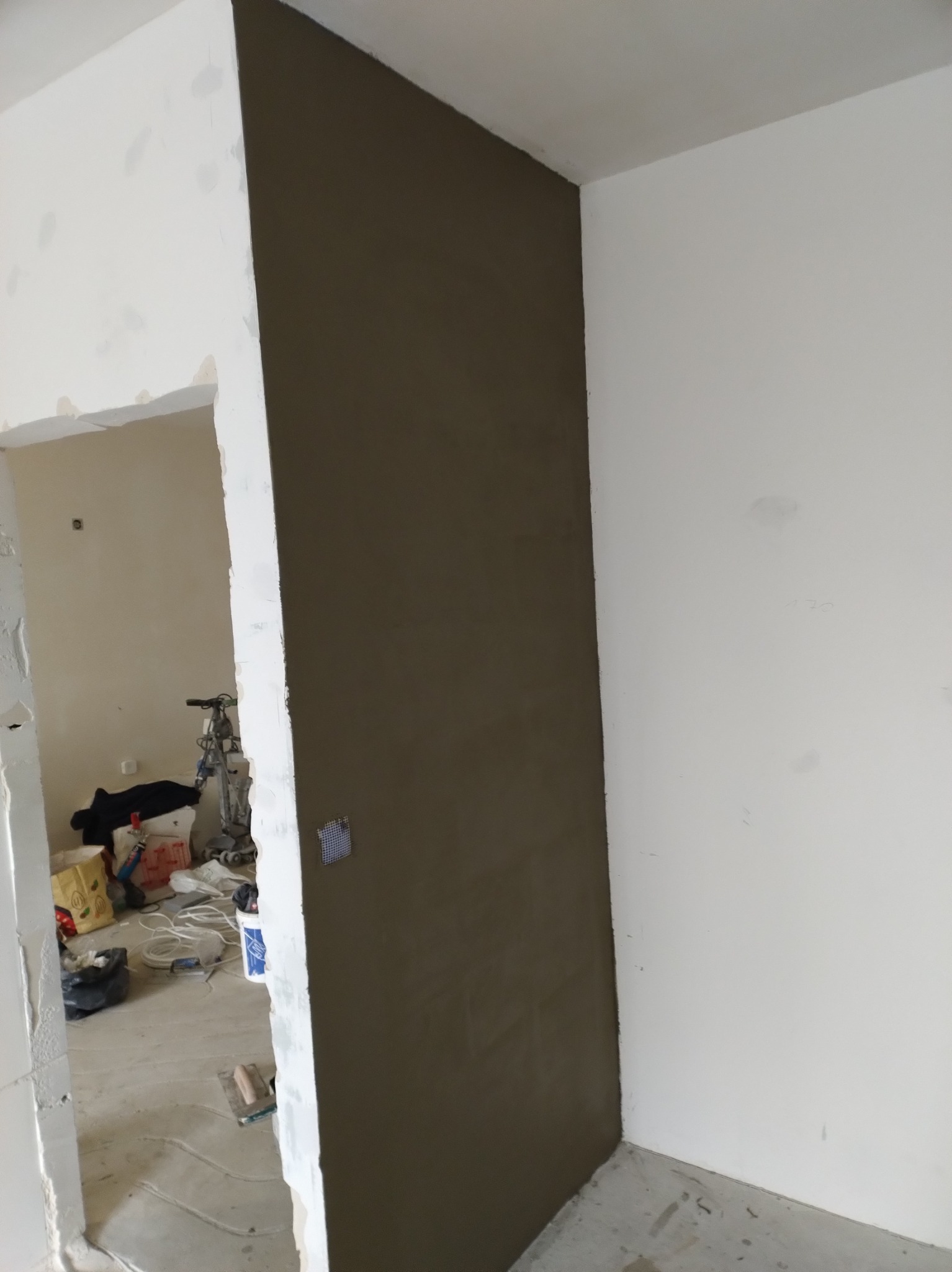 Ściana po nałożeniu gładzi szpachlowej w trakcie remontu mieszkania. Widoczny fragment pomieszczenia z przygotowanym podłożem i narzędzia szpachlarskie.