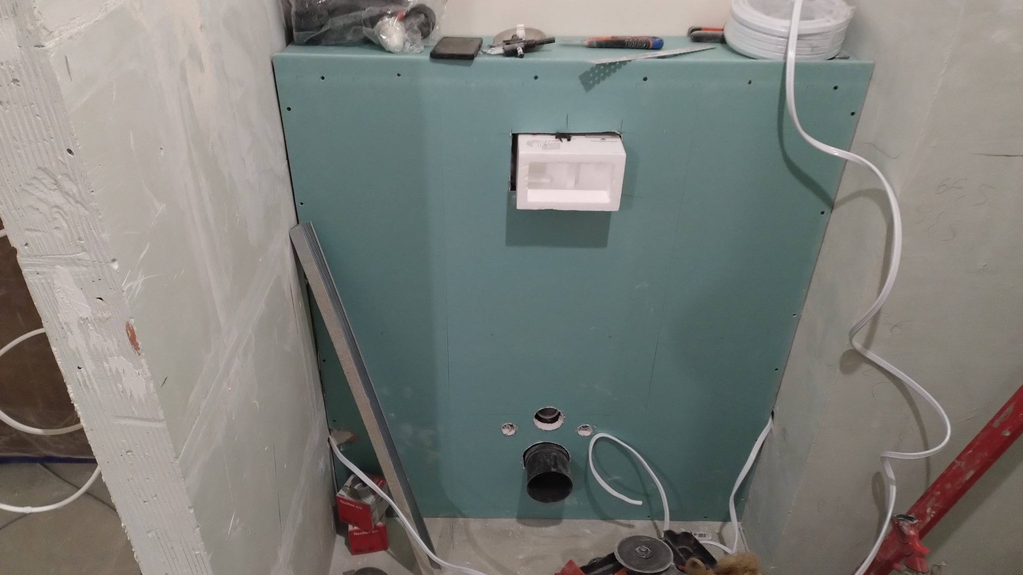 Zabudowa toalety podtynkowej z płyt gipsowo-kartonowych w trakcie montażu. Widoczne narzędzia, rura kanalizacyjna i elementy konstrukcyjne. Prace wykończeniowe łazienki.